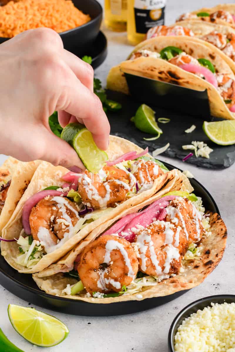 Easy Shrimp Tacos on black plate with lime juice being squeezed on top.
