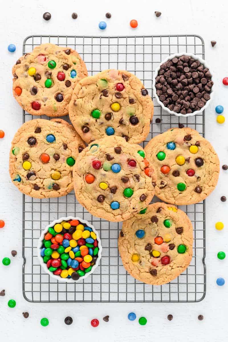 Overhead shot of Best Big Fat Chewy Chocolate Chip M&M Cookies on cooling rack with bowls of M&M's and chocolate chips nearby.