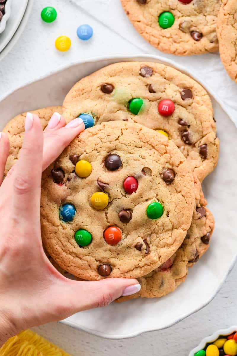 Overhead shot of hand grabbing one Best Big Fat Chewy Chocolate Chip Cookie from platter.