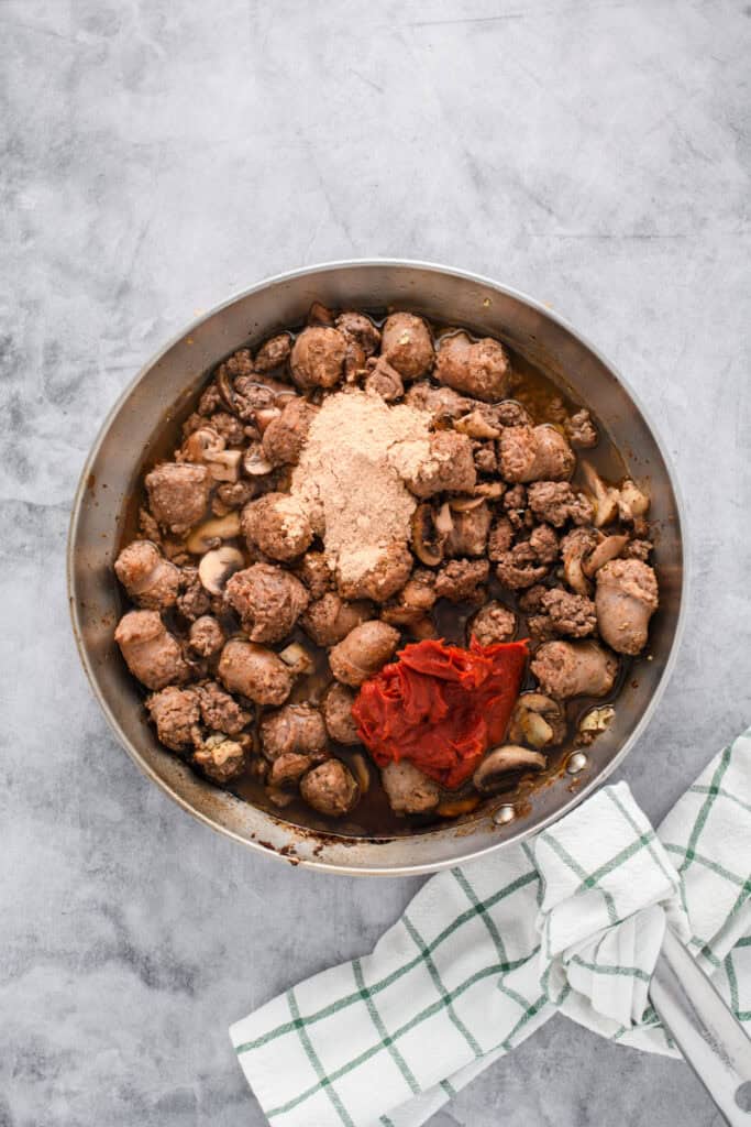 Overhead shot of tomato paste, spices and water in saute pan for Italian Sausage Spaghetti.