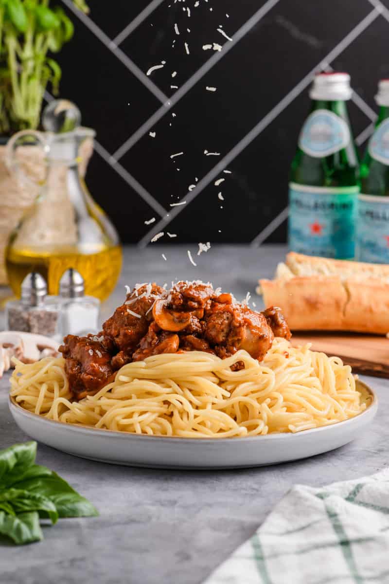 Head on angle of Italian Sausage Spaghetti on a plate with Parmesan cheese falling on top.