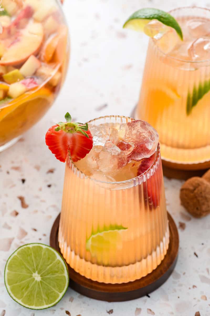 Angled shot of a glass of Sparkling Sangria with second glass and pitcher in the background.