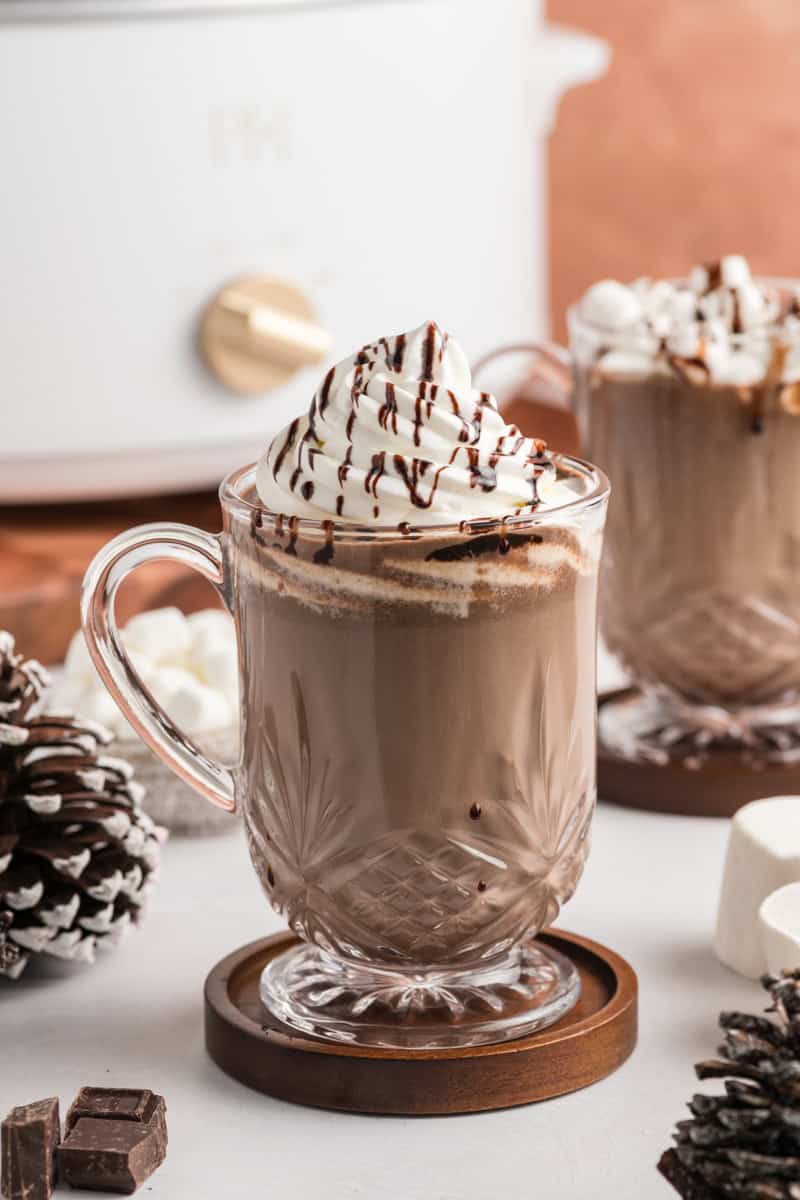 Cup of Slow Cooker Hot Chocolate with slow cooker in the background with additional cup of hot chocolate.
